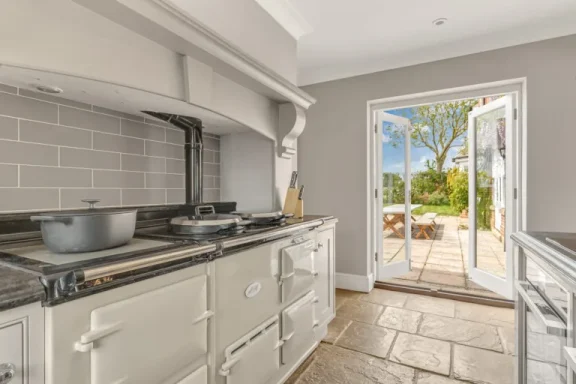 Bright kitchen with an AGA stove, leading to a garden view through open doors.